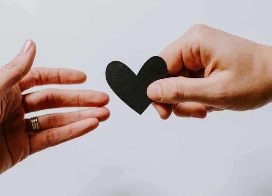 A photo of a hand giving a heart cutout to another hand.