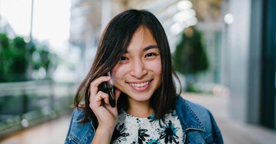 An Asian woman smiling at the camera while holding her phone.